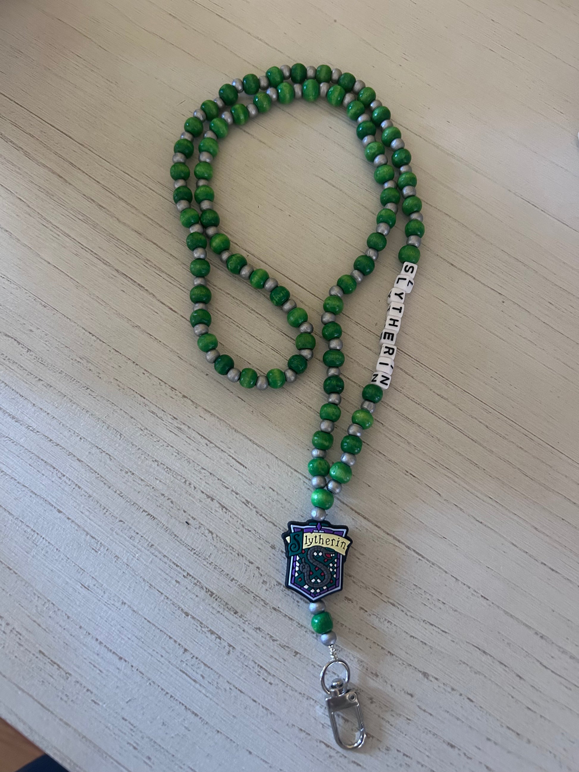 Green beaded lanyard with a badge holder on a light wooden surface